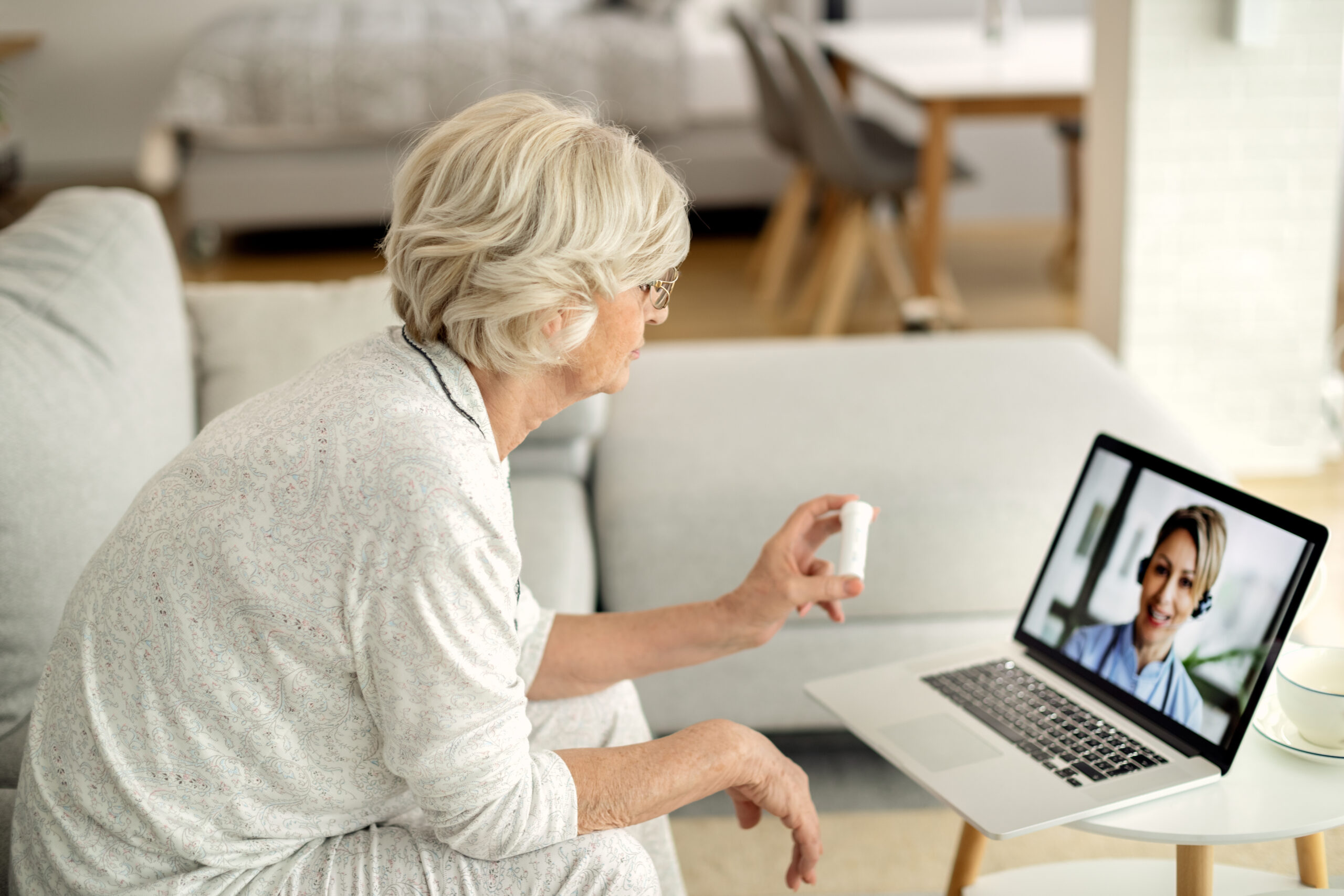 Senior woman using laptop while having video call with her doctor and talking about a medicine.